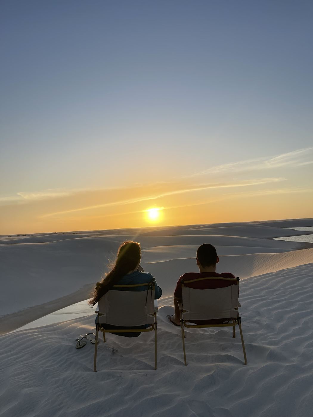 Casal vendo o pôr do sol sentado nas dunas